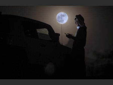A man looks at his phone as a "supermoon" rises over the desert near Tabuk, some 1500 kilometers northwest of the Saudi capital Riyadh, on November 14, 2016.  The phenomenon happens when the moon is full at the same time as, or very near, perigee -- its closest point to Earth on an elliptical, monthly orbit. It was the closest to Earth since 1948 at a distance of 356,509 kilometres (221,524 miles), creating what NASA described as "an extra-supermoon". / AFP PHOTO / Mohammed Albuhaisi