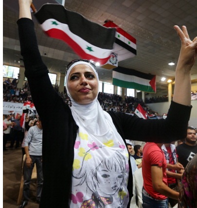A Syrian woman holds a natinoal flag under a poster bearing portraits of President Bashar al-Assad during a meeting gathering workers in his support ahead of the upcoming presidential elections on May 13, 2014 in the capital Damascus. The campaign for Syria's elections that started this week, has become a tribute to incumbent Bashar al-Assad, and in the streets of Damascus, residents have little doubt who will win the June poll. AFP PHOTO/ LOUAI BESHARA (Photo credit should read LOUAI BESHARA/AFP/Getty Images)